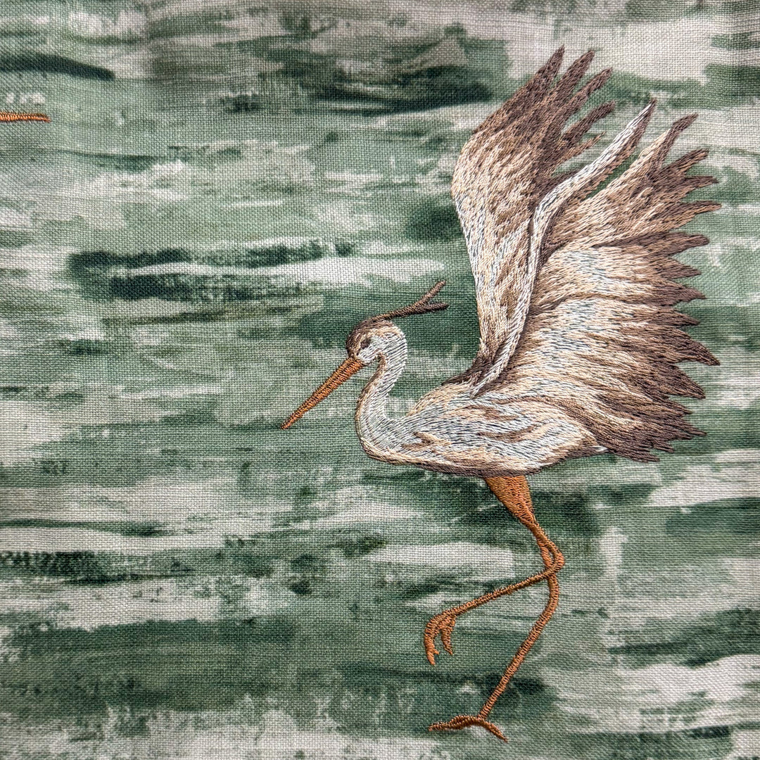 Embroidered heron on fabric with a textured green background