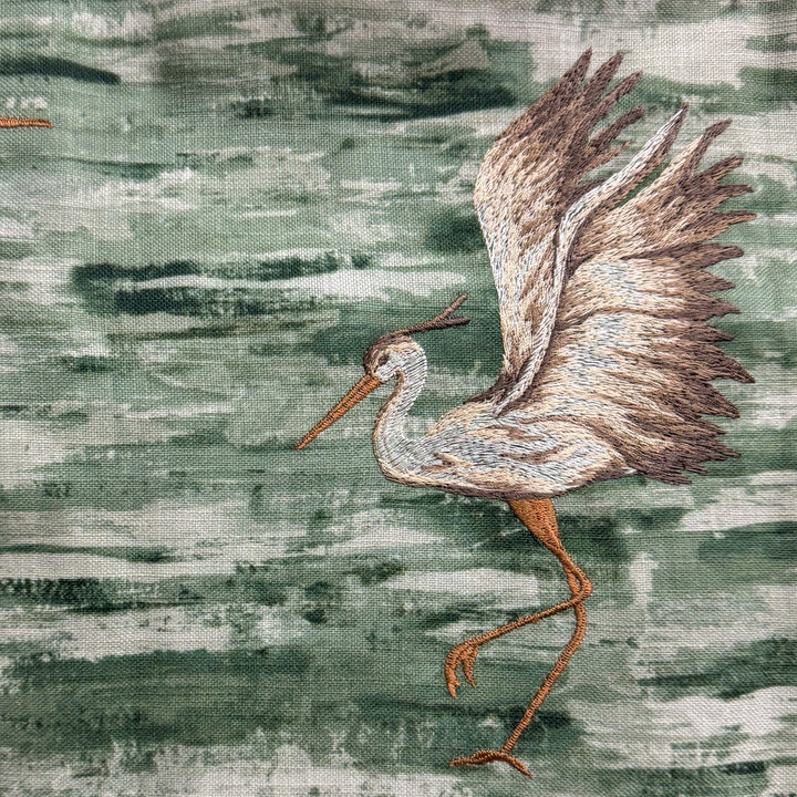 Embroidered heron on fabric with a textured green background
