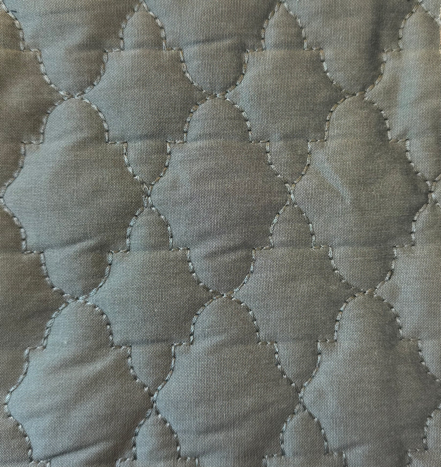 Quilted fabric with a geometric pattern in shades of green.