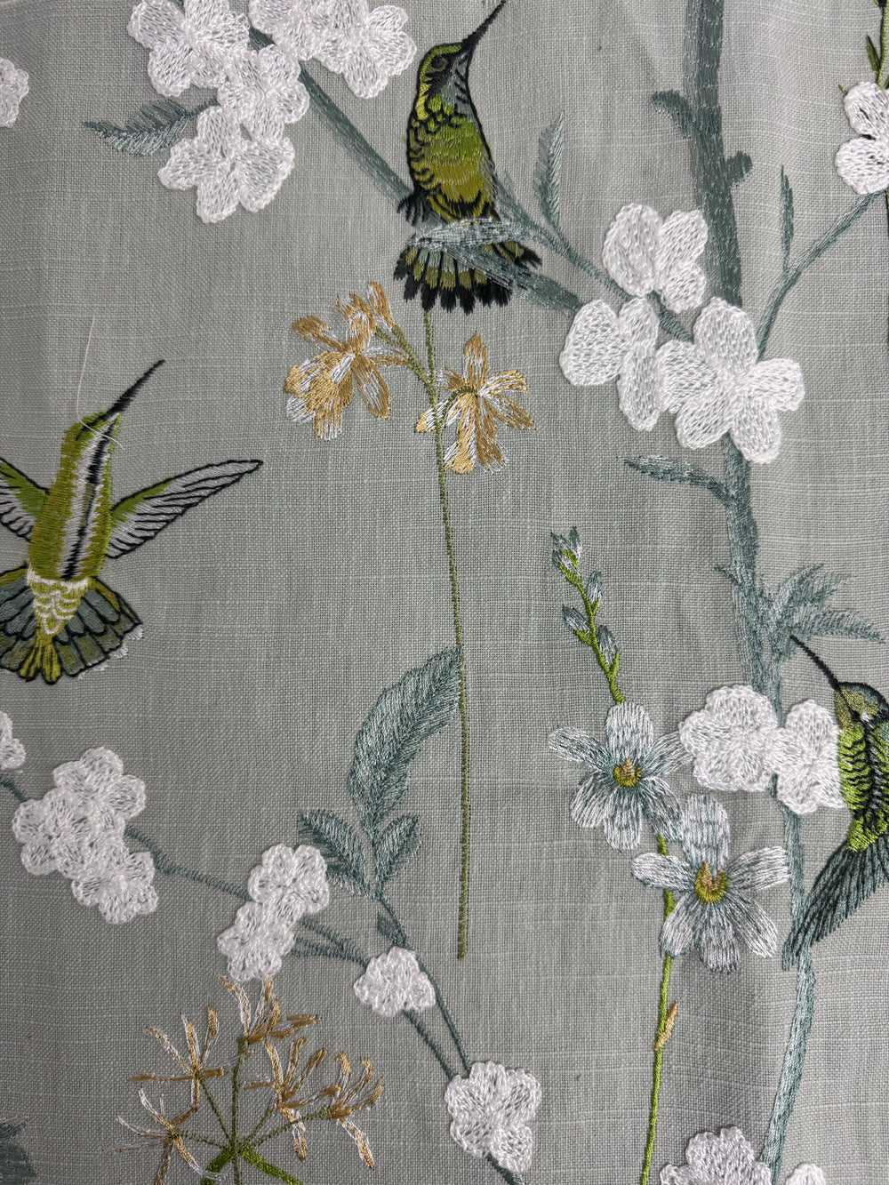 Textile with embroidered hummingbirds and flowers on a gray background