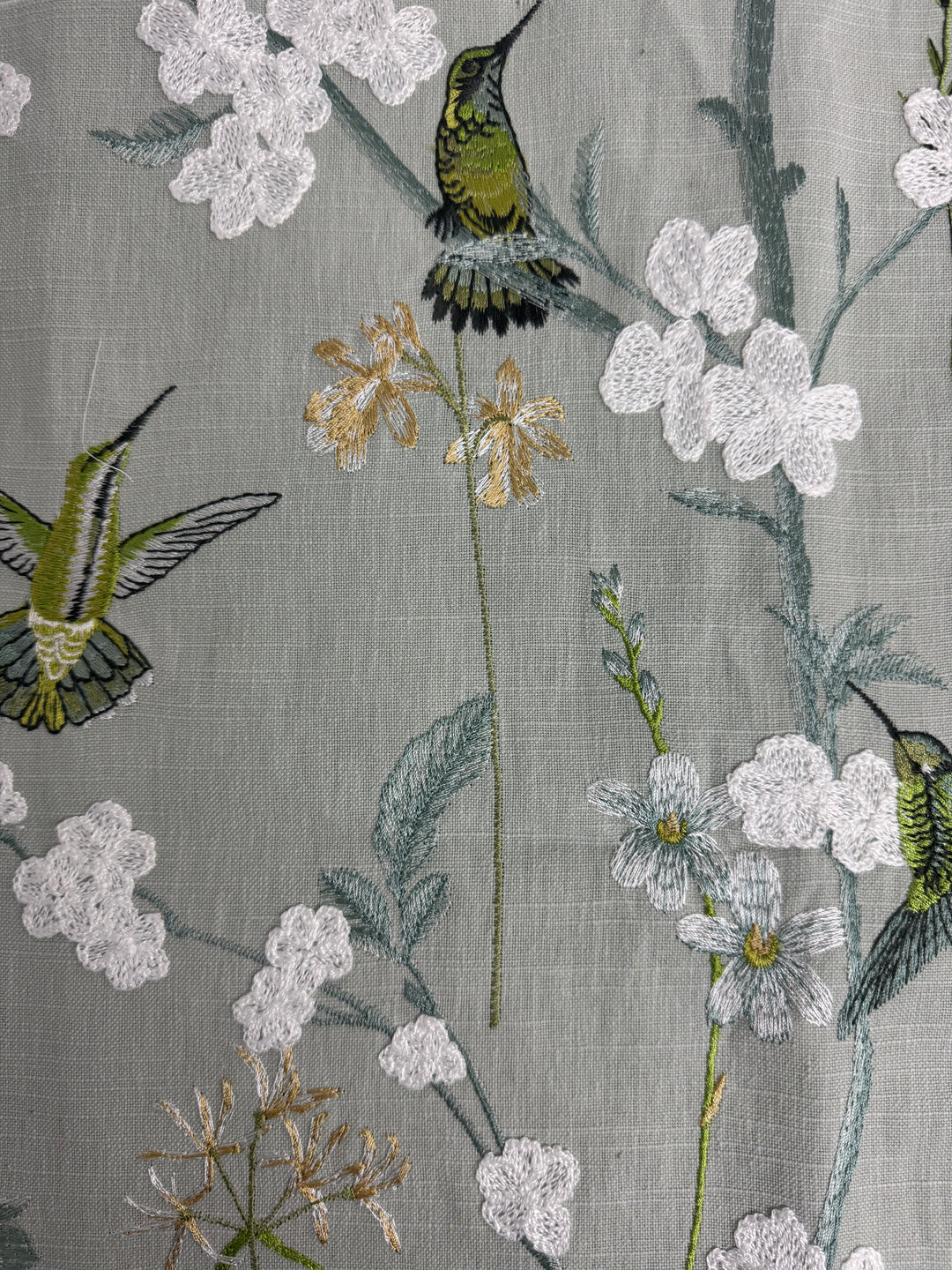 Textile with embroidered hummingbirds and flowers on a gray background