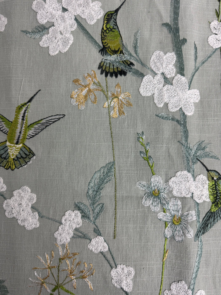 Textile with embroidered hummingbirds and flowers on a gray background