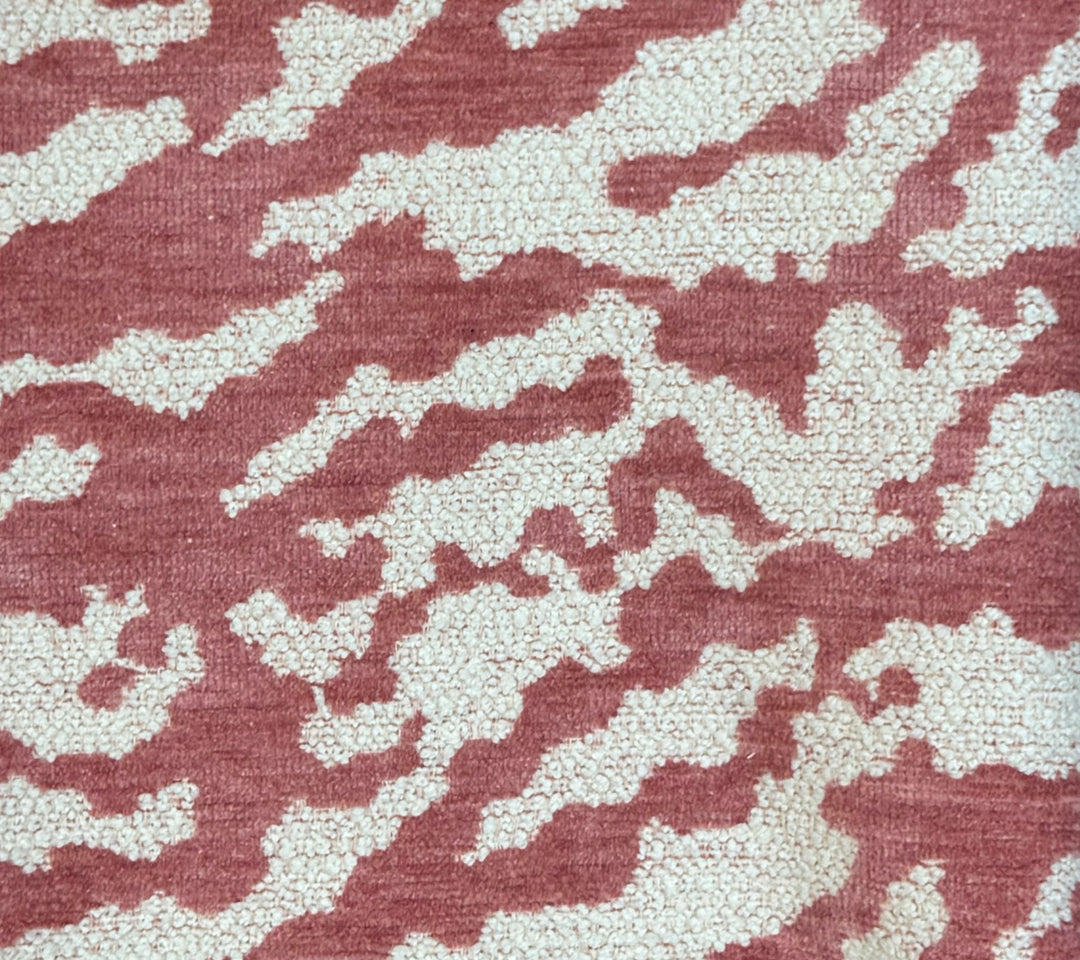 Close-up of a textured fabric or carpet pattern with an abstract organic design in dusty rose pink and off-white.