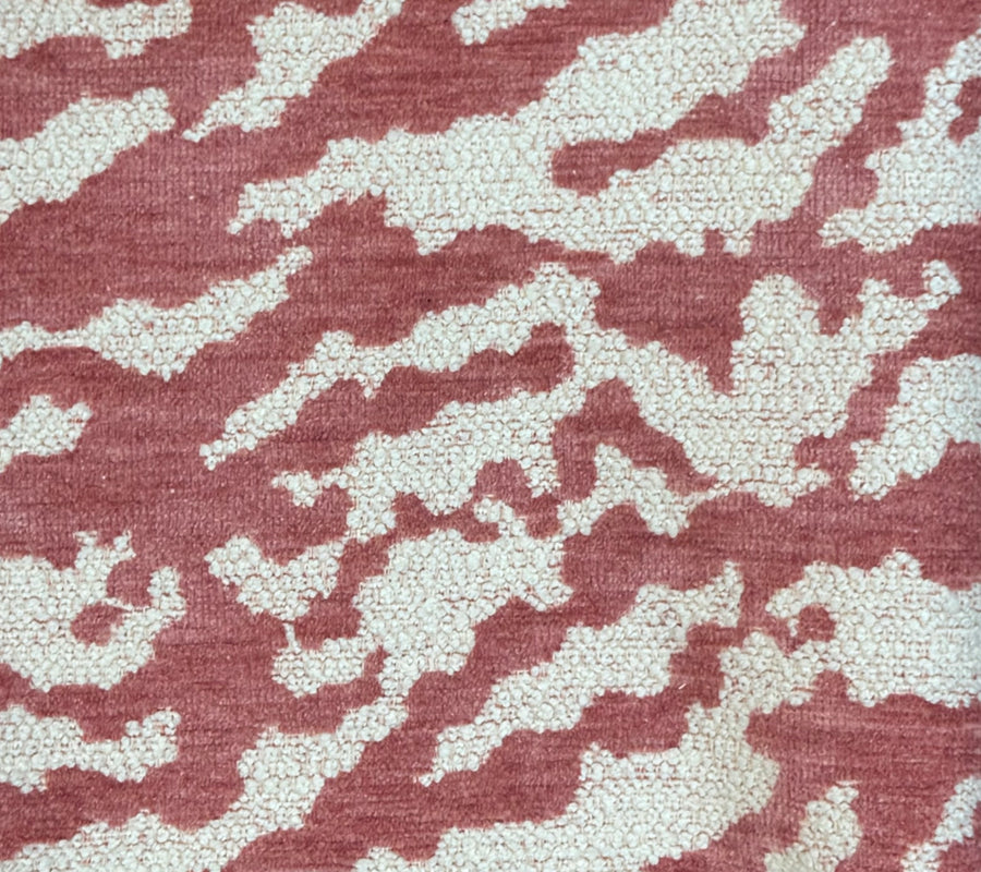Close-up of a textured fabric or carpet pattern with an abstract organic design in dusty rose pink and off-white.