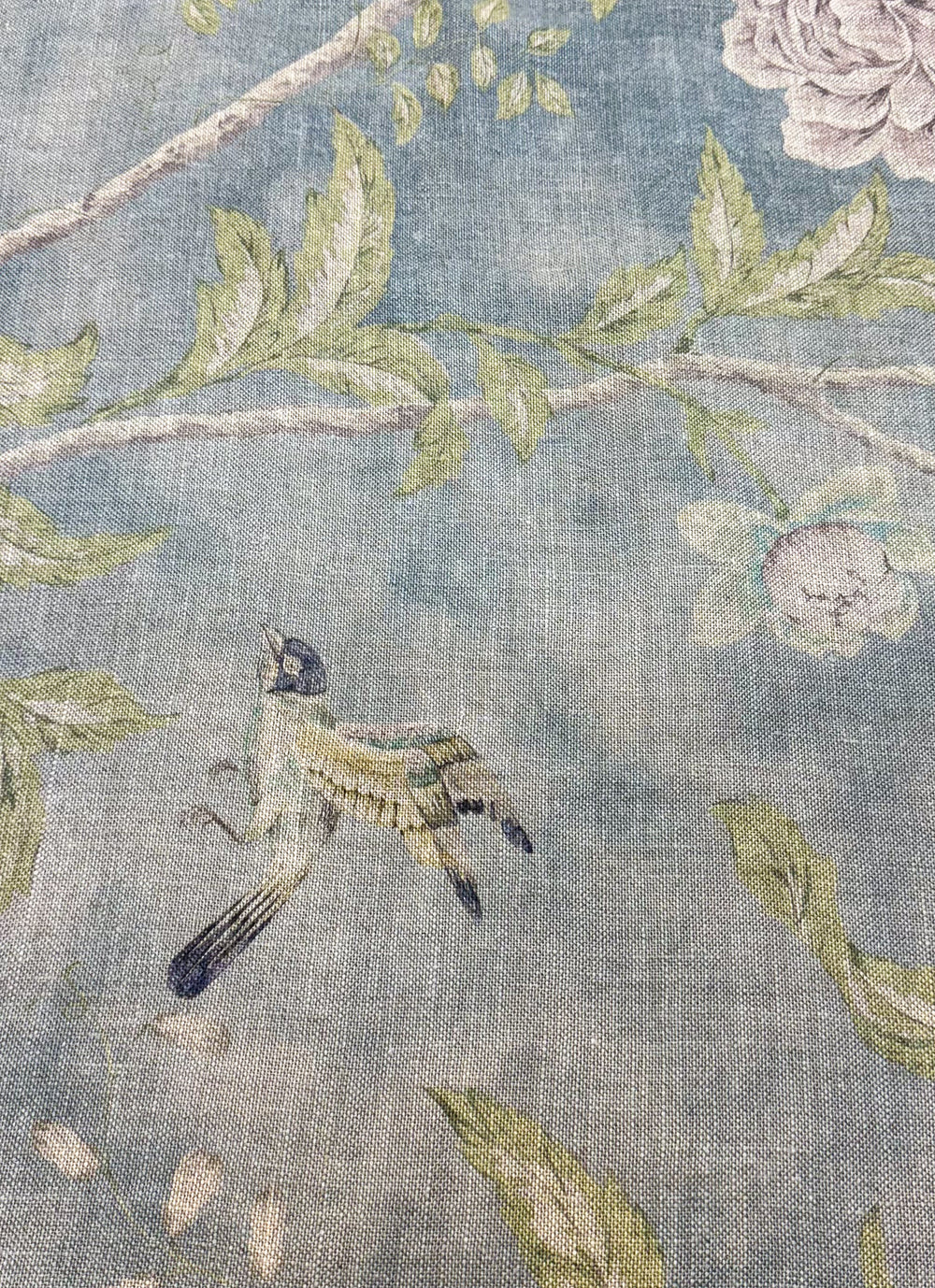 A close-up view of a blue linen fabric with a floral and bird pattern.