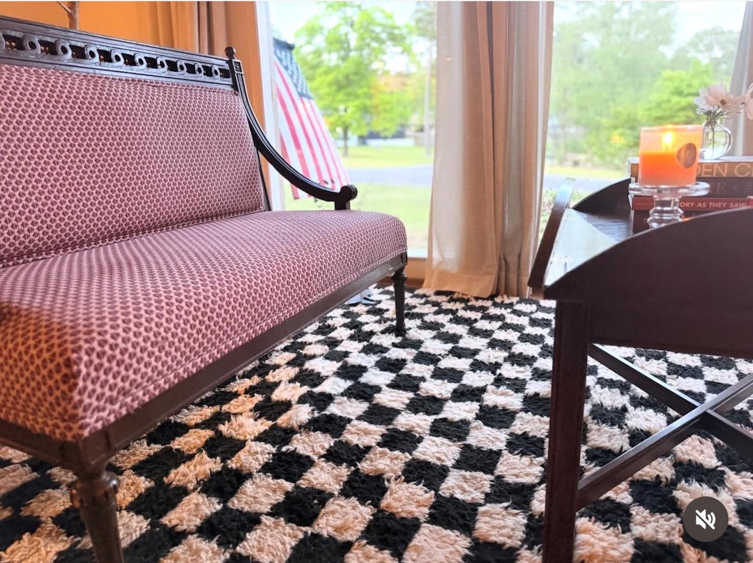 Living room with a checkered rug, pink sofa, and a table with a drink.