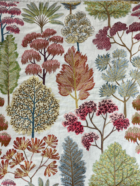 Fabric with an embroidered floral pattern featuring a variety of trees and shrubs in shades of blue, green, orange, pink, and yellow on a natural beige background.